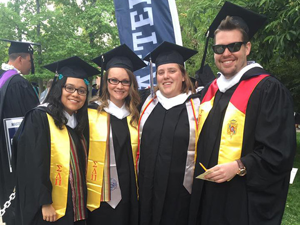 Spanish graduate students stand on quad wearing commencement attire