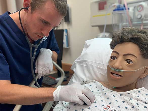 a male nursing student listening to the heartbeat of a male simulation mannequin