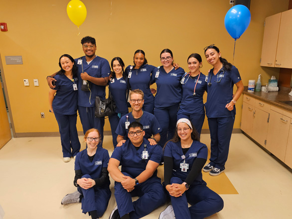 A group of Orvis School of Nursing students wearing blue scrubs pose for a group photo with two students holding a balloon.