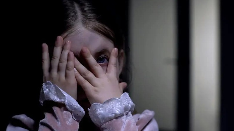 An afraid young girl holding her hands over her face.