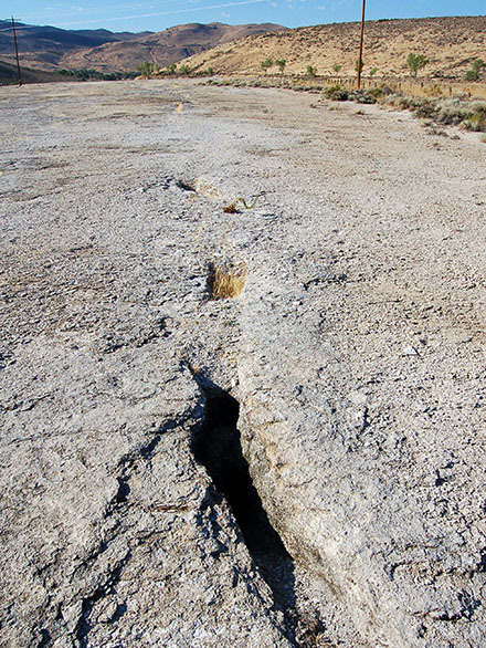 An open fissure in silica is pictured on a road surrounded by tall brown grass.