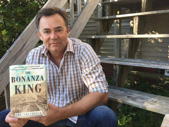 Photo of author Gregory Crouch seated on chairs and holding his book, The Bonanza King