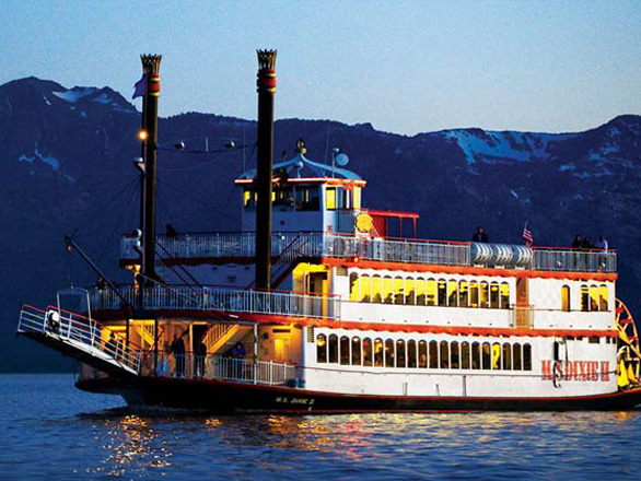 The MS Dixie, the famous paddleboat, sails across the blue waters of Lake Tahoe as evening settles and turns the skies and Sierra mountains a light shade of blue.