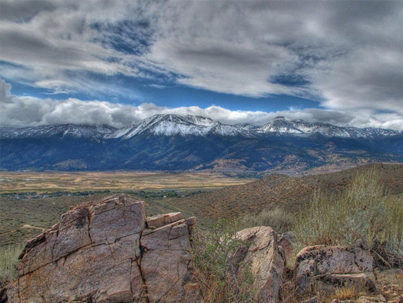 Rock formations sit in Washoe Valley Nevada, with the sagebrush desert stretching to the horizon with mountain ranges extending up to a cloudy sky.