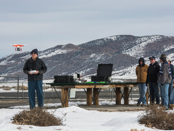 A group watches on as a man flies a drone with a mountain backdrop.