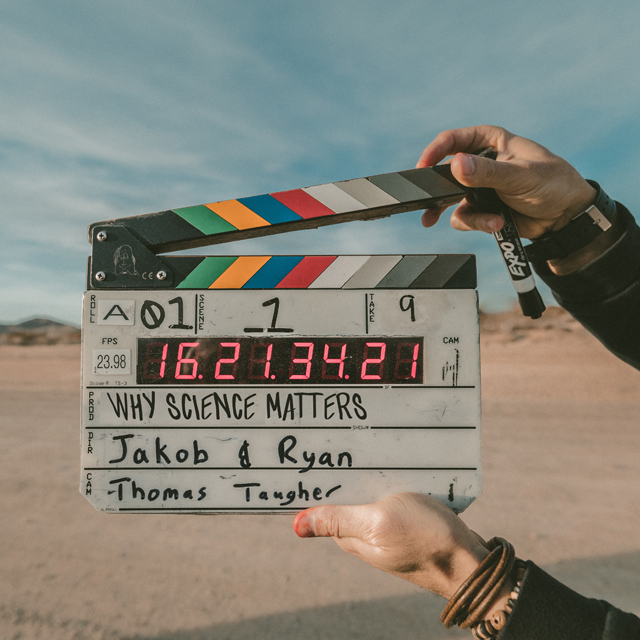A person holds a clap board in the desert with a light blue sky above