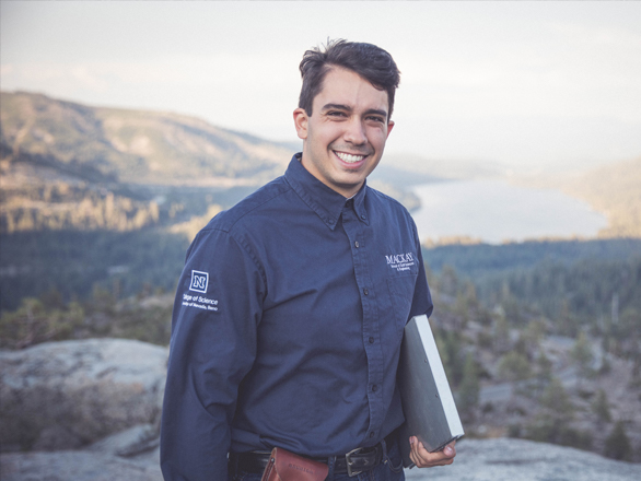 Portrait of a student wearing a Mackay shirt standing above a lake overlook holding a clip board.