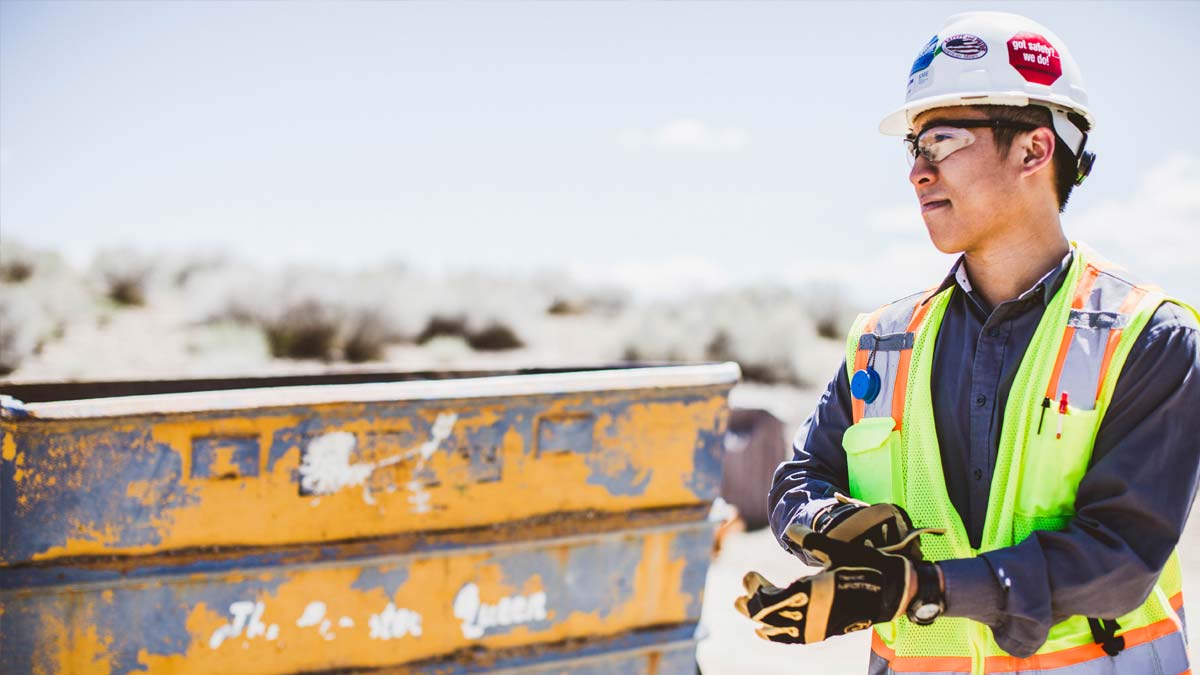 A mining engineering student wearing a hardhat and vest near an outdoor work site