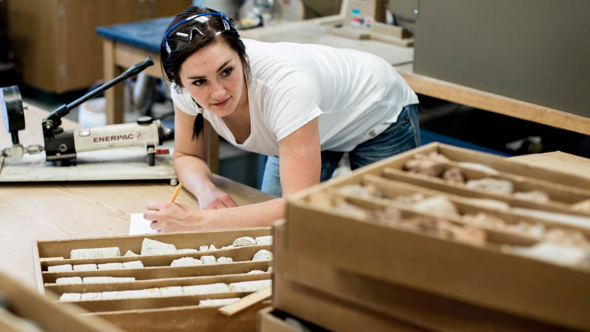 A student looks at rock samples and takes notes in a lab