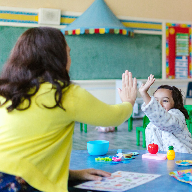 Teacher in a classroom high-fiving one of her students for a job well done.