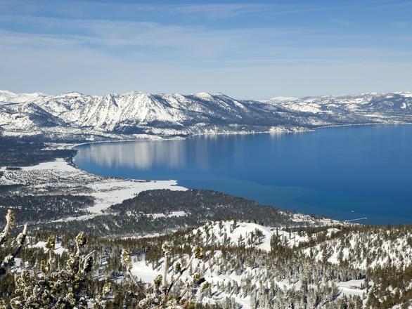 Aerial view of snow and forest surrounding Lake Tahoe.
