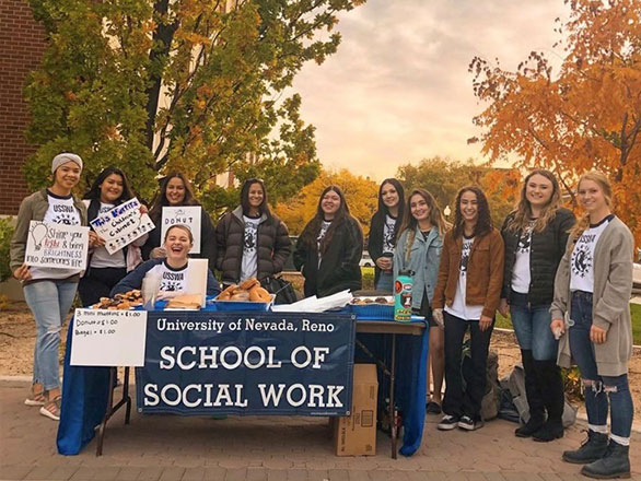 a group of students standing around a table with a sign that says School of Social Work