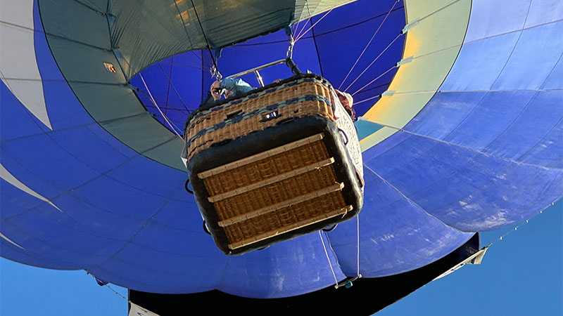Upward view of a hot air balloon basket, equipment, person and balloon.