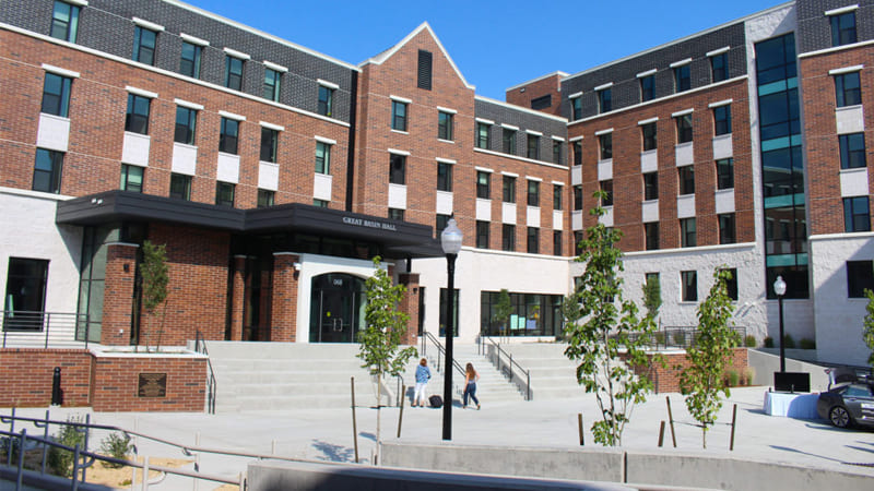 Two people walk up the concrete steps to Great Basin Hall, a brick covered residence hall with numerous windows on the second floor
