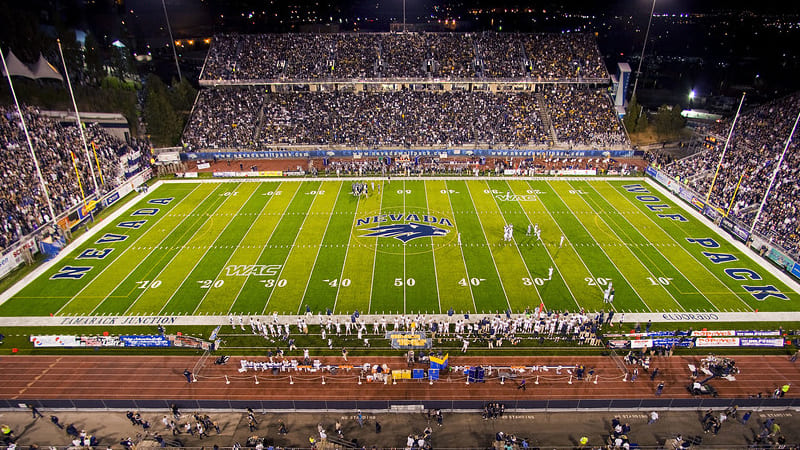 Thousands of fans fill the seats at Mackay Stadium to watch a football game, with the green turf and sport wolf logo at the 50-yard line