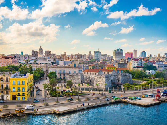 Vibrant Havana skyline featuring colorful buildings, historic architecture, and lively waterfront along the harbor under a blue sky.