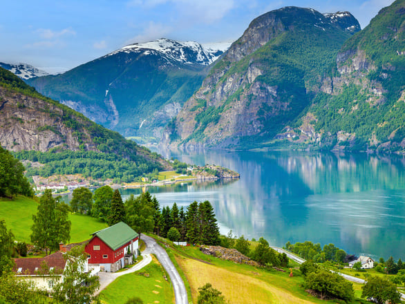 Sognefjord with a red house and green roof on the left and a body of water on the right in front of the green mountains.