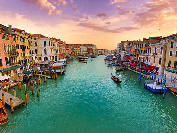 Gondolas float in a river between two rows of buildings in Italy.