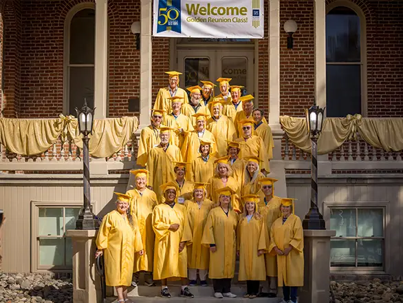 Members of the 2023 Golden Reunion class wear gold graduation attire and pose for a photo on the steps of Morrill Hall.