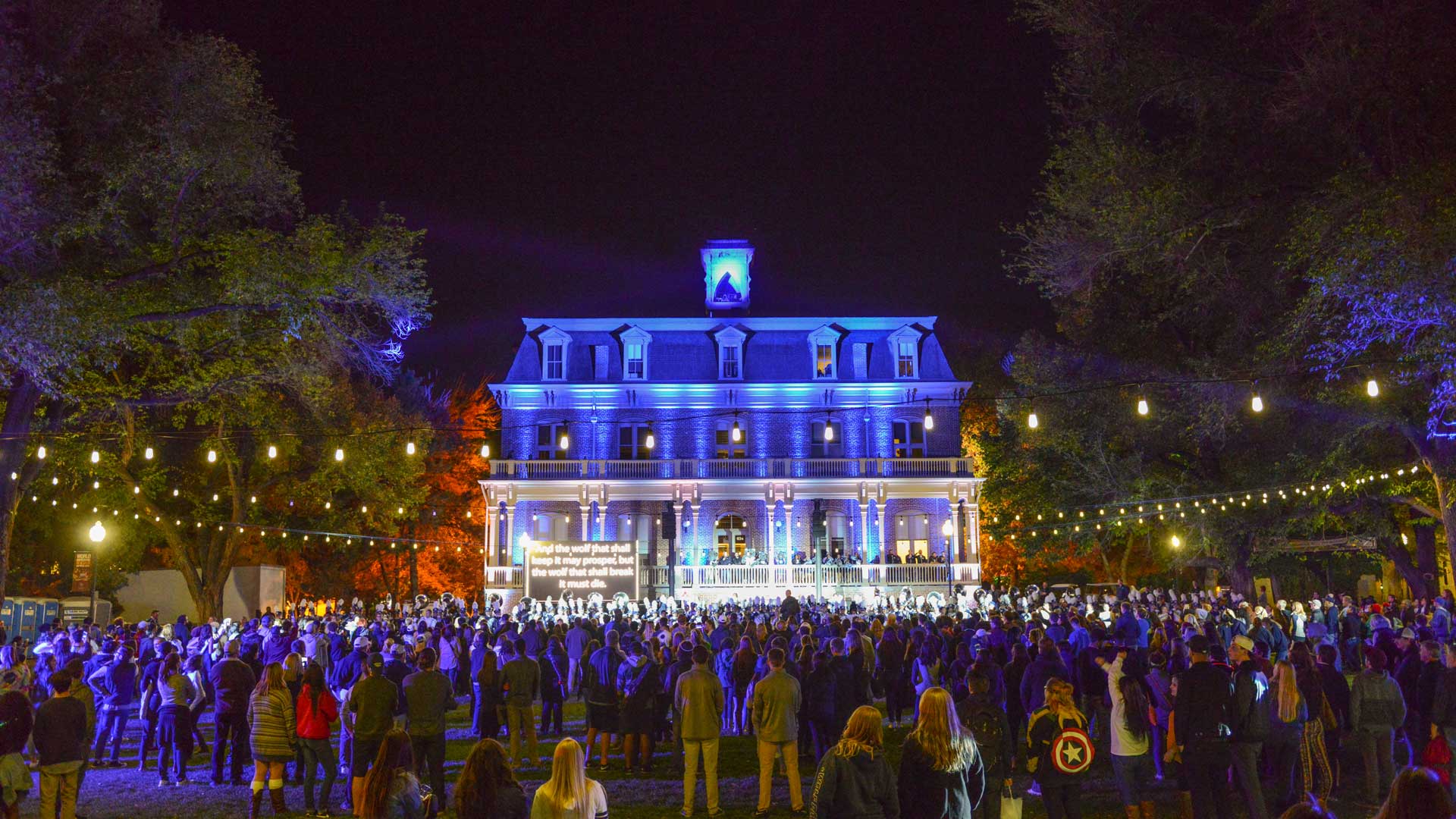 Event on the quad at night with a crowd of people and Morrill Hall lit in blue