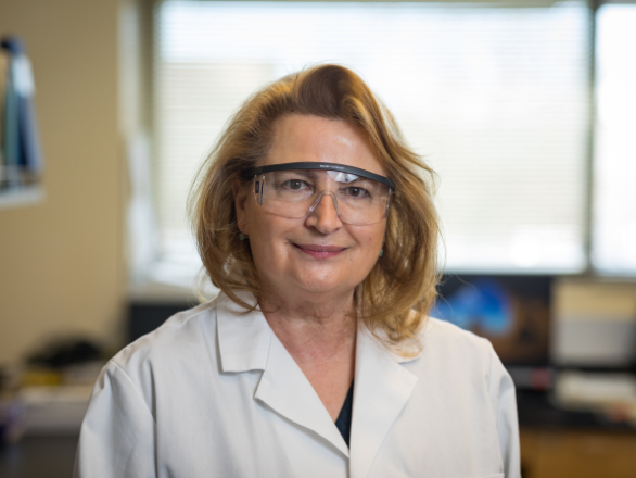Woman in lab coat and safety glasses smiling for photo.