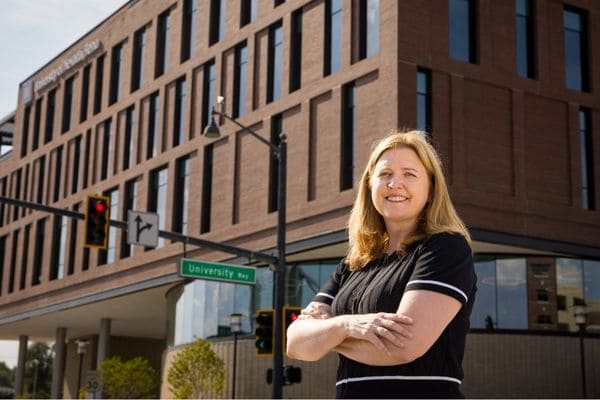 A woman stands in front of the John Tulloch Business Building, partially visible in the frame.