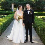 Kate Levia (left) wears a wedding dress while standing next to her husband, wearing a tux, Yonatan Levia.