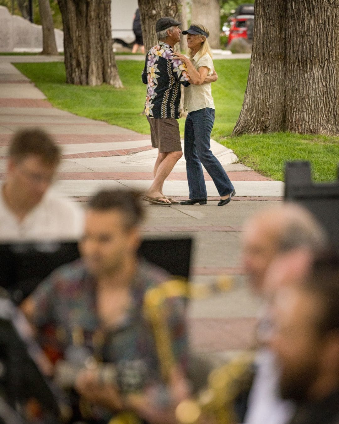 A couple joyfully dancing together in a sunny park, surrounded by trees and greenery.