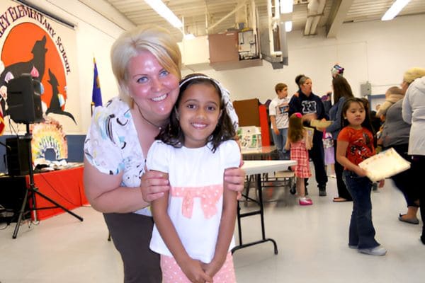 A woman and a young girl stand together in a cozy room, smiling and enjoying each other's company.
