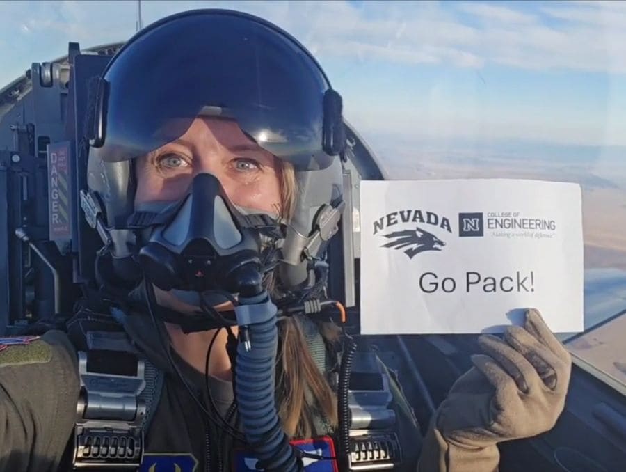 Inside a fighter jet, a woman displays a sign saying “Go Pack!” 