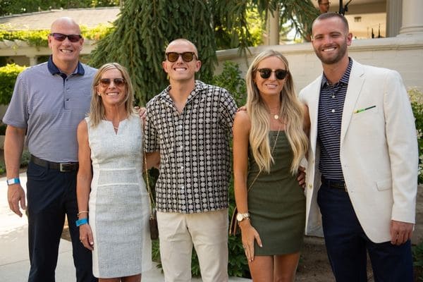 A group of five nicely dressed individuals smiling and posing for a photo at an event.   