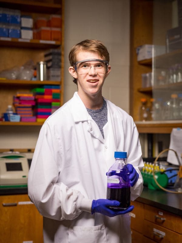 University science student poses for a photo holding a purple dye.