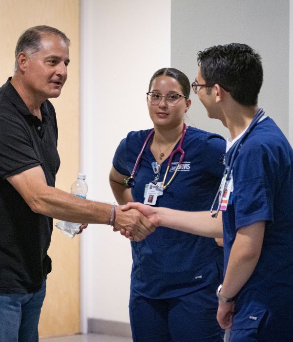 Medical student and teacher shake hands while other student watches the interaction.