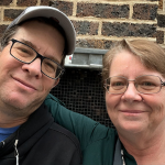 Robert Moore wears glasses and a hat and poses next to Elizabeth Moore (wearing glasses).