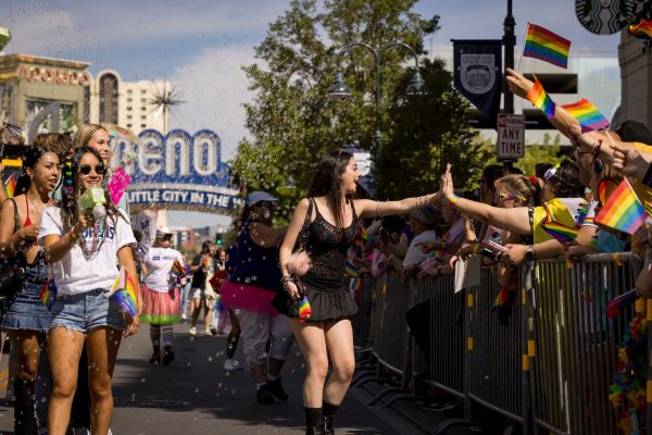 A lively scene at a pride parade in Reno, with participants and spectators exchanging high-fives. People hold rainbow flags, symbolizing LGBTQ+ pride.