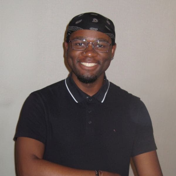 Smiling person wearing glasses, a black bandana, and a dark collared shirt against a neutral background, conveying a friendly and cheerful mood.
