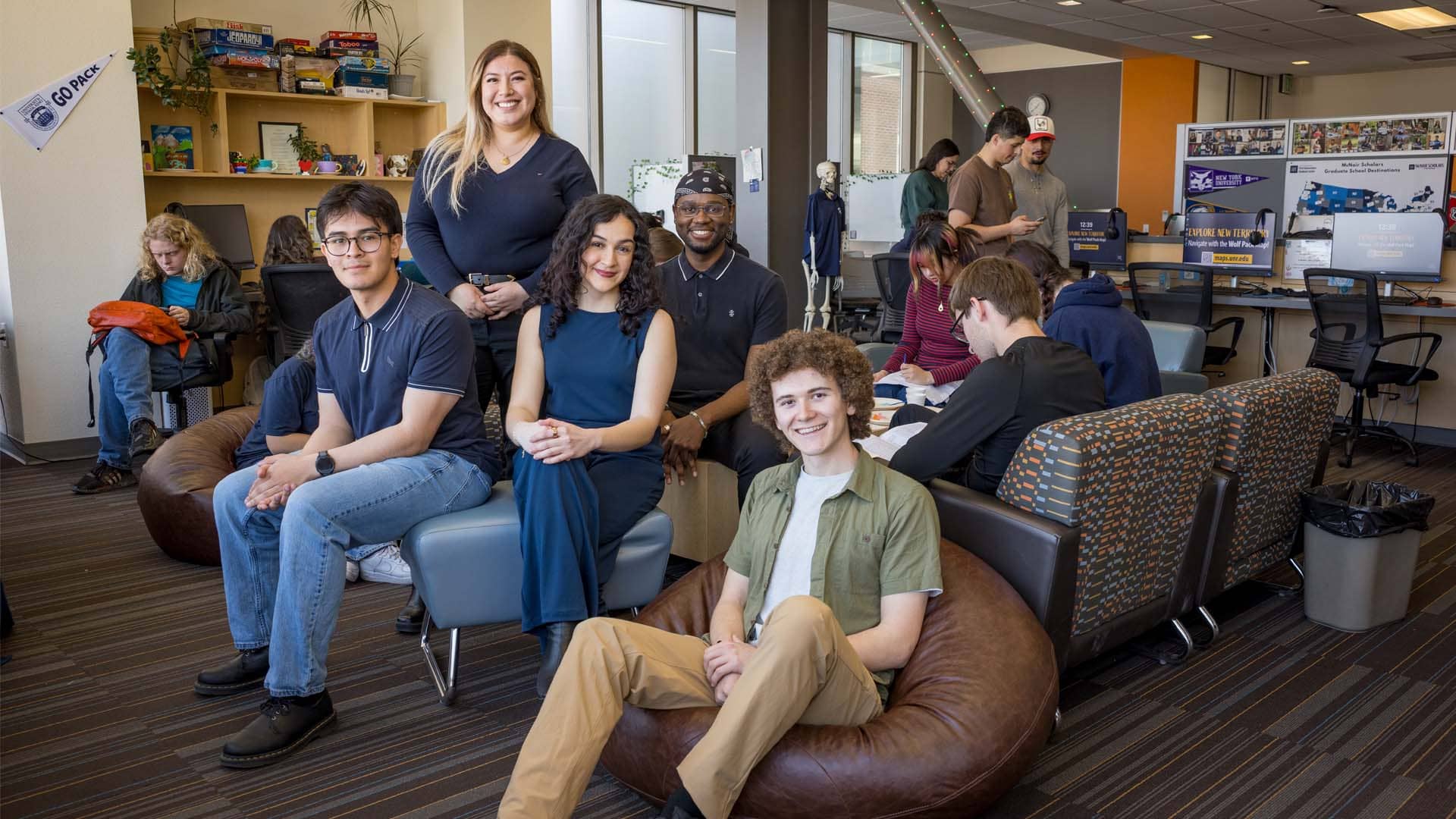 A group of people sit casually in a modern lounge, conversing and relaxed. Bean bags, couches, and computers create a collaborative atmosphere.