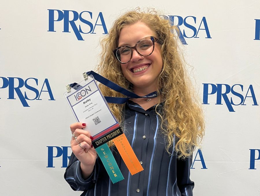 Kolby KingKing flashes her attendee badge at the 2025 PRSA ICON conference in Washington, D.C., Oct. 2025. Courtesy Kolby King. holds a PRSA conference badge. The background features a PRSA logo. The mood is professional and celebratory.