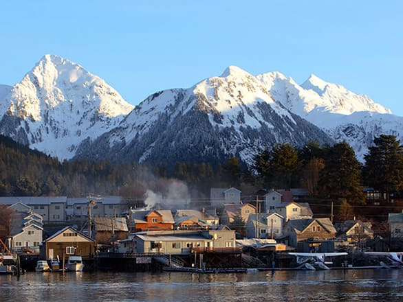 A small cold town next to the ocean in front of a snowy mountain range.