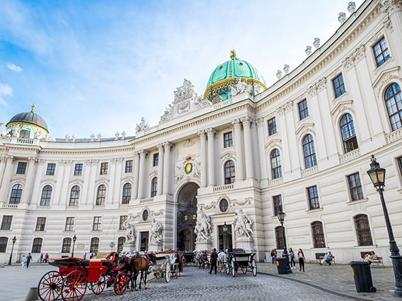 A large white building with gold details and statues with multiple red and white carriages in front.