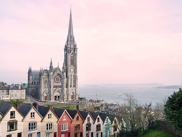 A line of colorful houses in front of a tall brown cathedral on the coast.