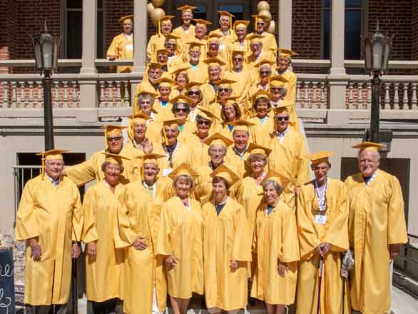 A group of graduates standing on the exterior steps of Morrill Hall in yellow gowns.