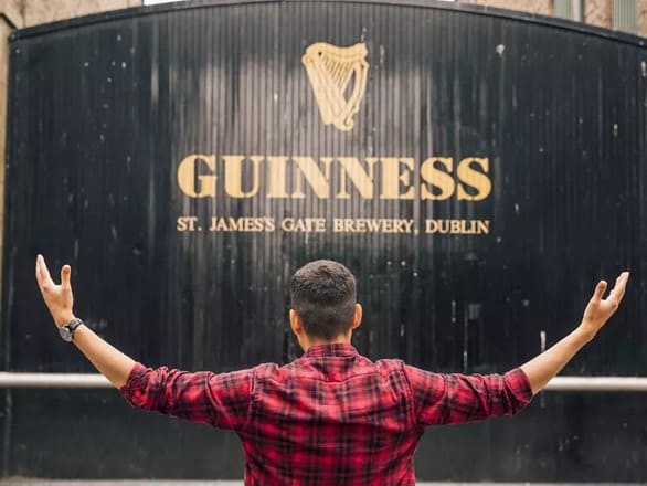 Man facing the Guinness wall with his arms up, welcoming it.