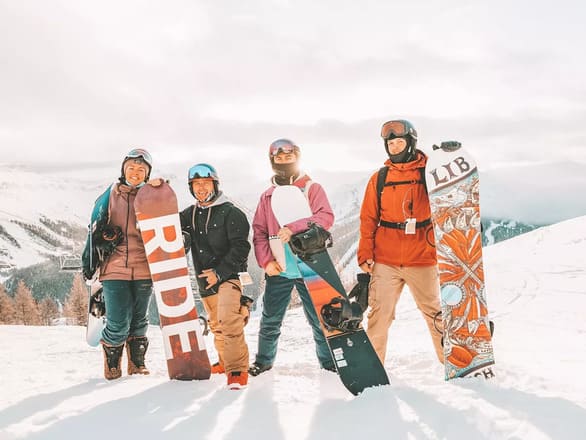 4 people posing on a snowy hill with their snowboards.