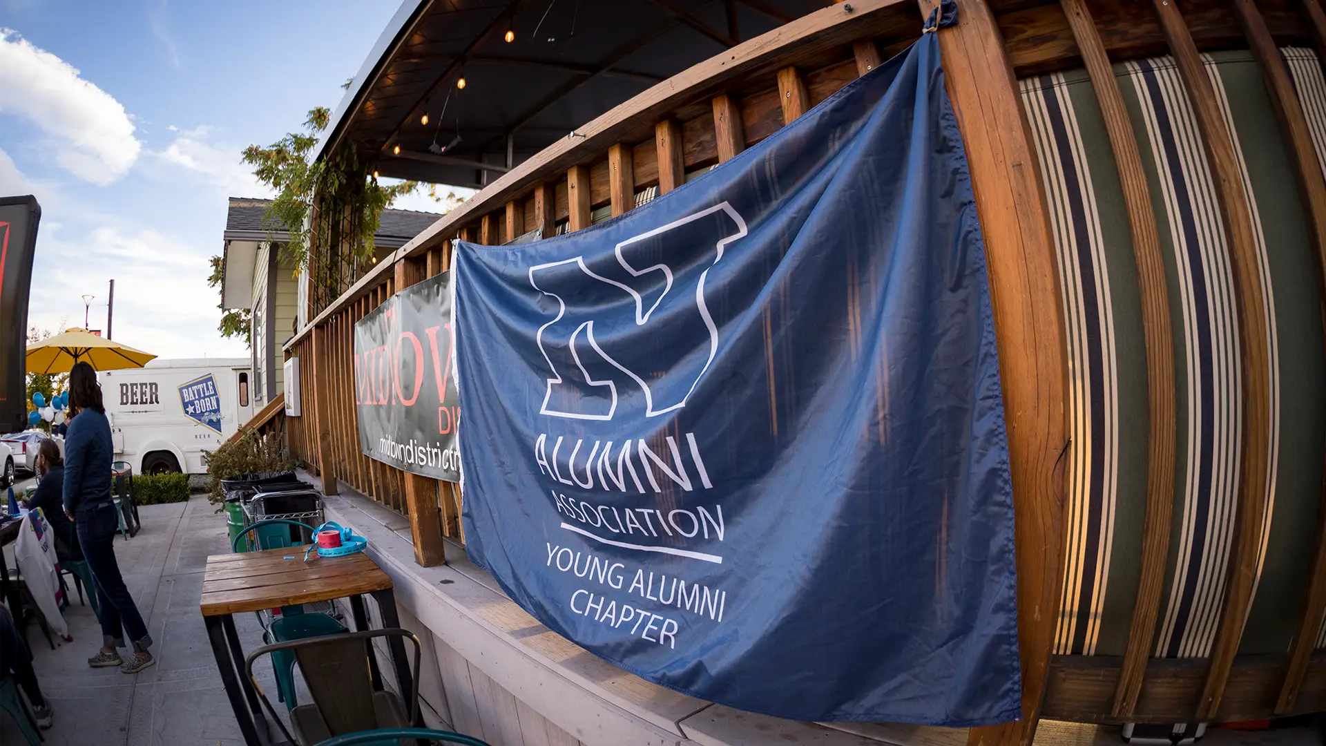 A banner with the Nevada Block N logo and the words "Young Alumni Chapter" hangs from a fence railing.