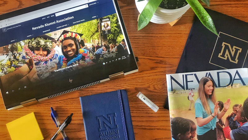 A desk showing an iPad with the Alumni website, a Nevada Silver & Blue magazine and other University of Nevada, Reno branded items