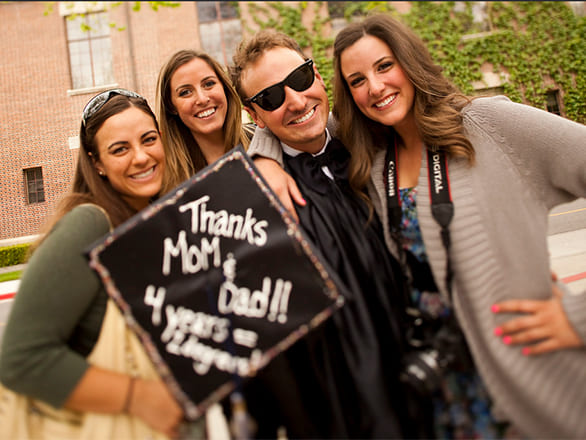 Graduate in regalia holding mortar board that says thanks mom and dad