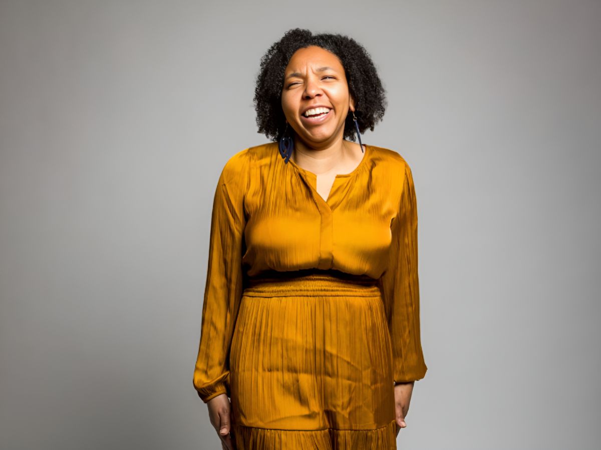 Monique Normand smiles while standing and wearing a gold dress.