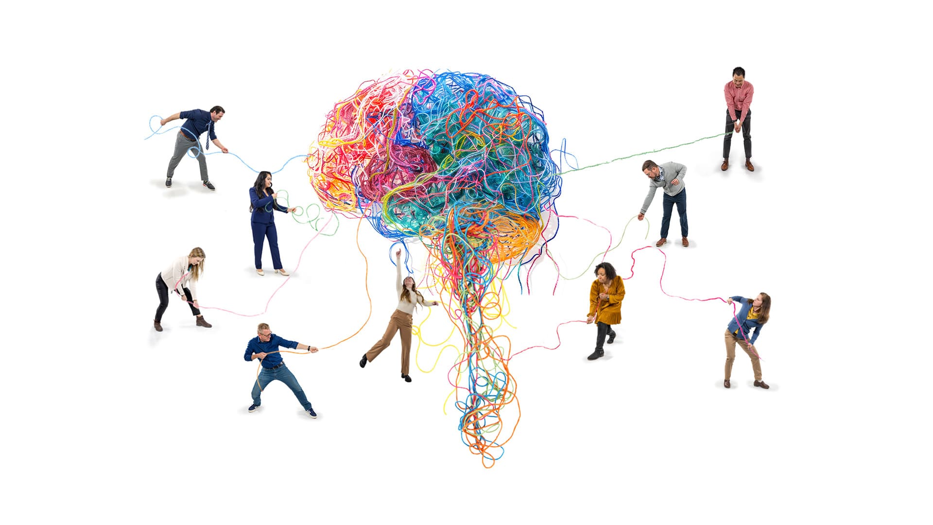 A group of people surround a giant multicolored ball of yarn shaped like a brain, pulling individual threads from the central structure.