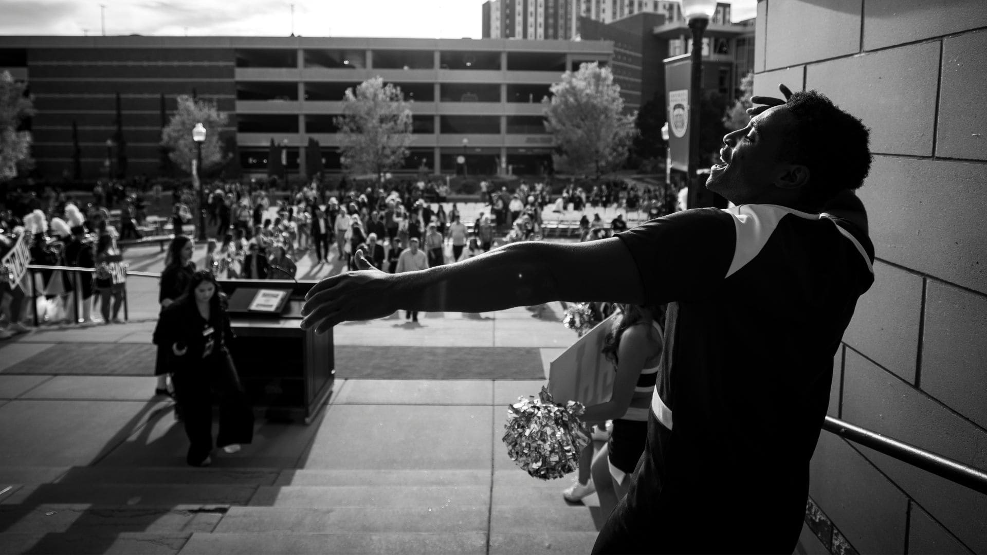 A man stands with arms wide open, positioned on stairs, expressing a gesture of invitation or celebration.